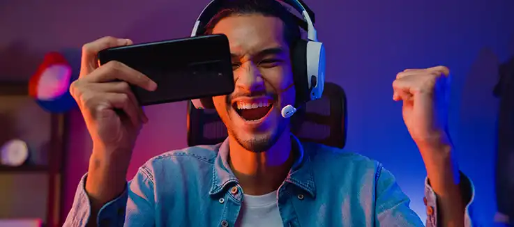 man wearing earphones celebrating a win on an online game on his phone.