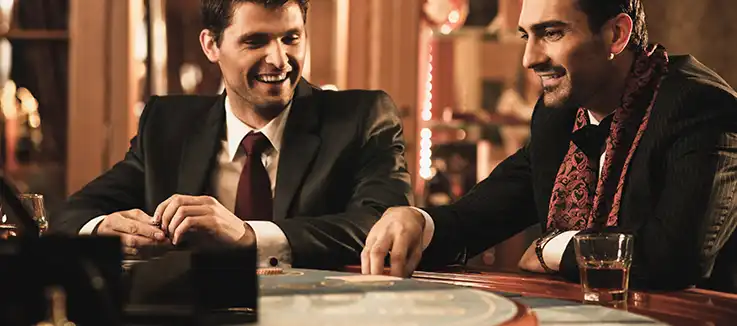 two men at a casino table with a drink